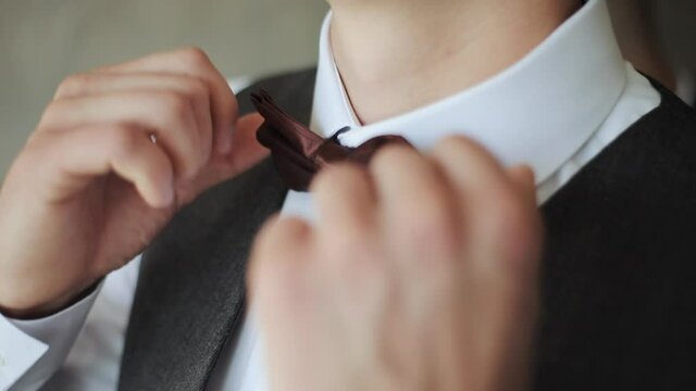 Close-up of man adjusting bow tie. Attractive man epicly adjusts bow tie on suit. Man straightens bow-tie. Success style confidence establishment luxury life concept.