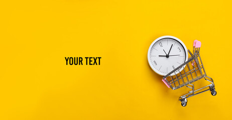 Shopping time. Supermarket trolley with clock on a yellow background. Minimalism. Top view. Copy...