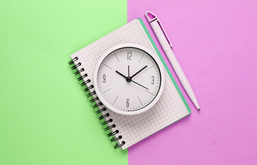 White clock and notebook on pink green pastel background. Minimalistic studio shot. Top view