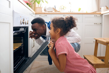 Father and kid cooking cakes in oven on breakfast