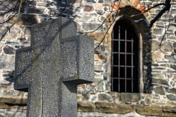 A stone cross in front of the church with a window.