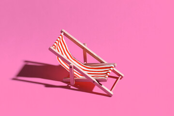 Mini beach deck chair on pink background with shadow. Sunlight. Symbol of beach holidays, resort. ...