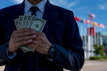 Happy business style holding dollars and calculating. Cheerful rich handsome businessman in counting money near business center background.