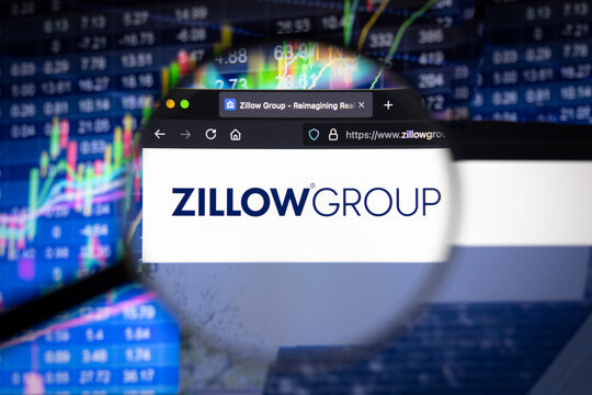 Zillow Group company logo on a website with blurry stock market developments in the background, seen on a computer screen through a magnifying glass