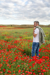 A man in a white t-shirt and jeans stands in a blooming poppy field and looks into the distance. 
Summer countryside vacation theme.