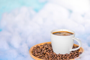 Cup of coffee and coffee beans on a round wooden tray, floating in the sky with white clouds. Copy space.