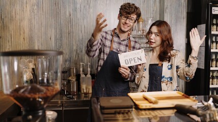 Business owner attractive young Asian woman in apron hanging we're open sign on front door  welcoming clients to new cafe. Happy waitess with protective face mask holding open sign at cafe .