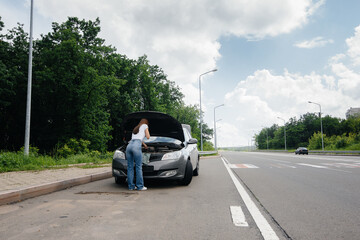 A young girl stands near a broken-down car in the middle of the highway and calls for help on the...