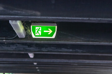 Naklejka premium Green exit sign with running person and green arrow shows guidance system signage in a parking lot for rescue and evacuation safety in dangerous situations at ceiling rescues life in extreme danger