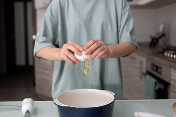 A woman in a t-shirt breaks a chicken egg in the kitchen and pours the egg white into a ceramic...