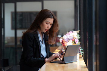 Asian businesswoman sitting at the counter working using a tablet in hand holding a smartphone at the office.