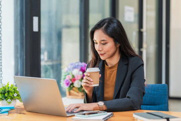 Fototapeta na wymiar Beautiful Asian businesswoman holding coffee sitting in an office chair using a laptop keyboard.