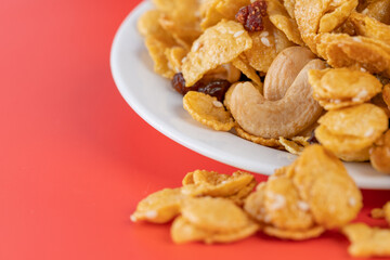 Cornflakes honey caramel homemade with grains, currant, cashew nut, dried strawberries and white sesame healthy food snack on a white plate close up and Macro copy space.