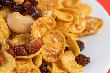 Cornflakes honey caramel homemade with grains, currant, cashew nut, dried strawberries and white sesame healthy food snack on a white plate close up and Macro copy space.