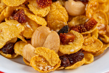Cornflakes honey caramel homemade with grains, currant, cashew nut, dried strawberries and white sesame healthy food snack on a white plate close up and Macro copy space.
