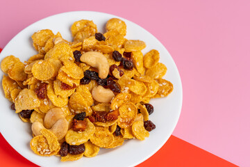 Cornflakes honey caramel homemade with grains, currant, cashew nut, dried strawberries and white sesame healthy food snack on a white plate close up and Macro copy space.