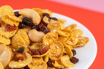 Cornflakes honey caramel homemade with grains, currant, cashew nut, dried strawberries and white sesame healthy food snack on a white plate close up and Macro copy space.