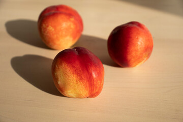 three ripe nectarines, peaches, lie on the light surface of a wooden table in the apartment. A charge of vivacity, vitamins, ripe fruits. Growing nectarine, pesticides