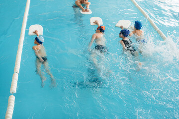 A group of boys and girls train and learn to swim in the pool with an instructor. Development of children's sports.