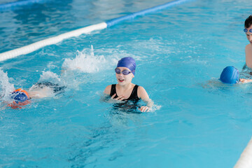 A group of boys and girls train and learn to swim in the pool with an instructor. Development of children's sports.