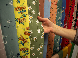 A large assortment of bright natural fabrics in the salon of textiles. A woman's hand selects...