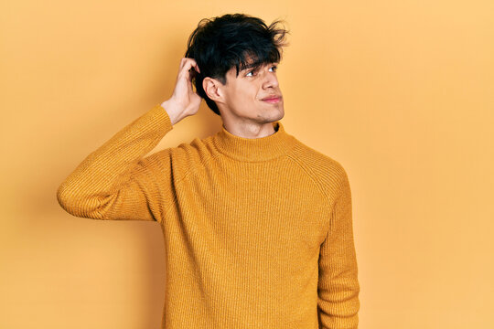 Handsome hipster young man wearing casual yellow sweater confuse and wondering about question. uncertain with doubt, thinking with hand on head. pensive concept.