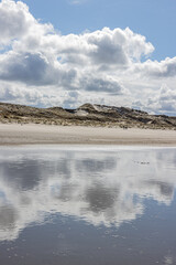 Water on the beach with mirror reflection of white clouds and dunes in the background, day with a blue sky and abundant clouds in Hargen aan Zee, North Holland, Netherlands. In time of coronavirus