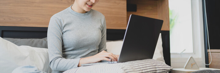 happy Young asian woman  working with laptop in bed at home in the morning
