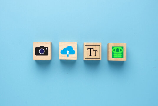 A picture of camera, upload, add title and earn money icon on wooden block. Be a stock photo and video contributor.