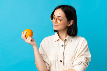 Young caucasian woman isolated on blue background holding an orange