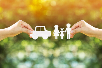 Woman hand holding a car and family model made of paper art filed together on nature bokeh in the...