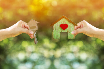 Women hand holding a home with red heart and a house-shaped keys filed together on nature bokeh in the public park, Loan for buy a house and real estate concept - Powered by Adobe