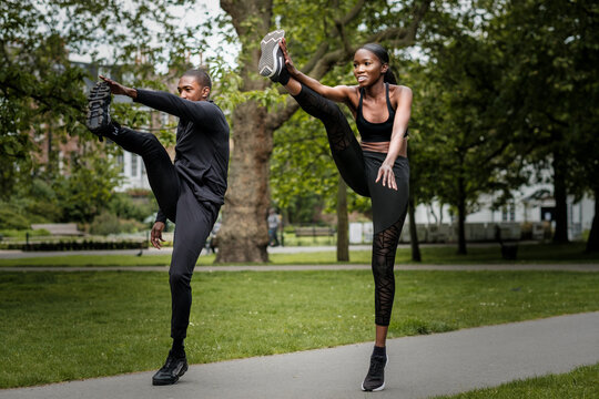 Black brother and sister twins doing exercise outdoors in stylish sportswear.