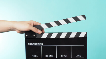 Fototapeta premium Hand is holding Black clapper board or movie slate on green or mint or Tiffany Blue background.