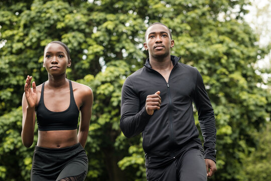 Black brother and sister twins running outdoors in stylish sportswear.