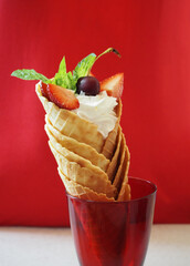 Summer dessert on red background, ice cream with fruits in waffle cones