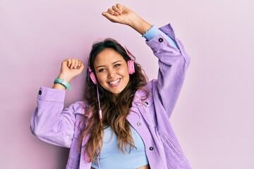 Young hispanic girl dancing and listening to music using headphones smiling with a happy and cool...