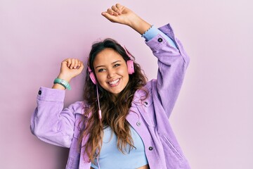 Naklejka premium Young hispanic girl dancing and listening to music using headphones smiling with a happy and cool smile on face. showing teeth.