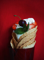 Summer dessert on red background, ice cream with fruits in waffle cones