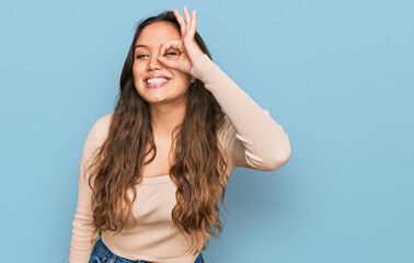 Fototapeta premium Young hispanic girl wearing casual clothes doing ok gesture with hand smiling, eye looking through fingers with happy face.