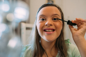 A latin girl with down syndrome putting on her make up with a smile.