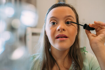 A latin girl with down syndrome putting on her make up with a smile.