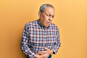Handsome senior man with grey hair wearing casual shirt with hand on stomach because indigestion,...