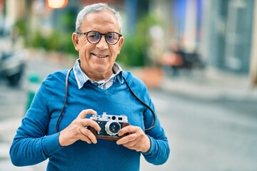 Senior grey-haired tourist man smiling happy using vintage camera at the city.