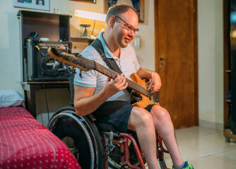 Young man using wheelchair playing on the bass guitar at bedroom