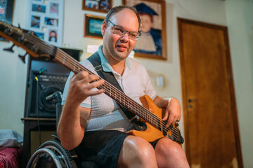 Young man using wheelchair playing on the bass guitar at bedroom