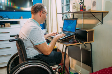 Latin man in wheelchair using laptop at home.