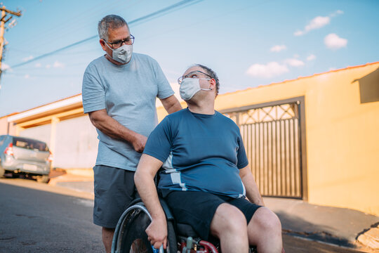 Father and son in wheelchair wearing face masks walking around town during the Covid-19 pandemic.