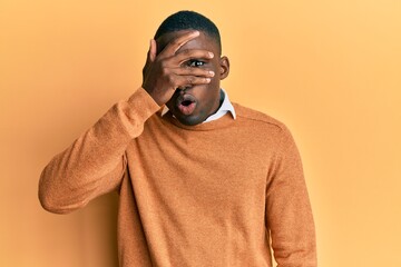 Young african american man wearing casual clothes peeking in shock covering face and eyes with hand, looking through fingers with embarrassed expression.