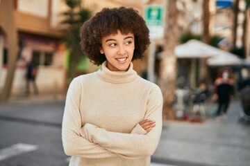 Young hispanic girl with arms crossed smiling happy at the city.